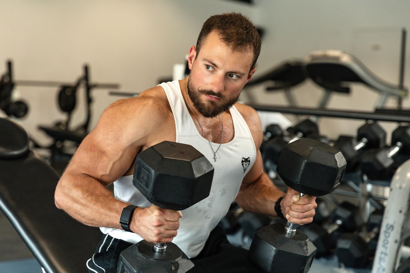 Sportif tenant deux haltères en salle de musculation, prêt pour une séance d'entraînement