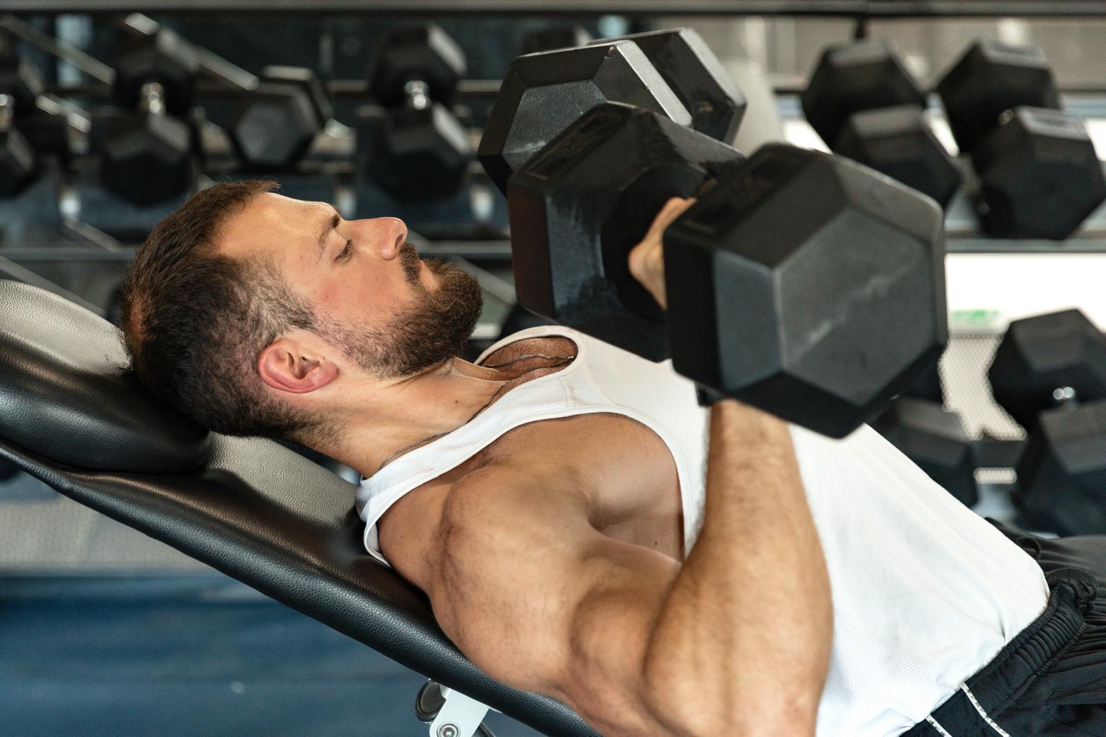 Homme réalisant un développé couché aux haltères en salle de musculation